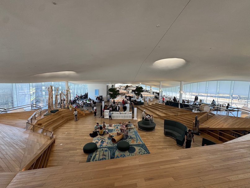 People read on steps and seats under the white wavy ceiling of the top floor of Oodi in Helsinki.