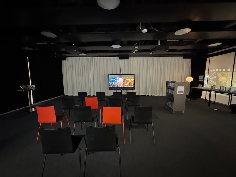 Black and orange chairs face a screen in a dark event room in Oodi library in Helsinki.