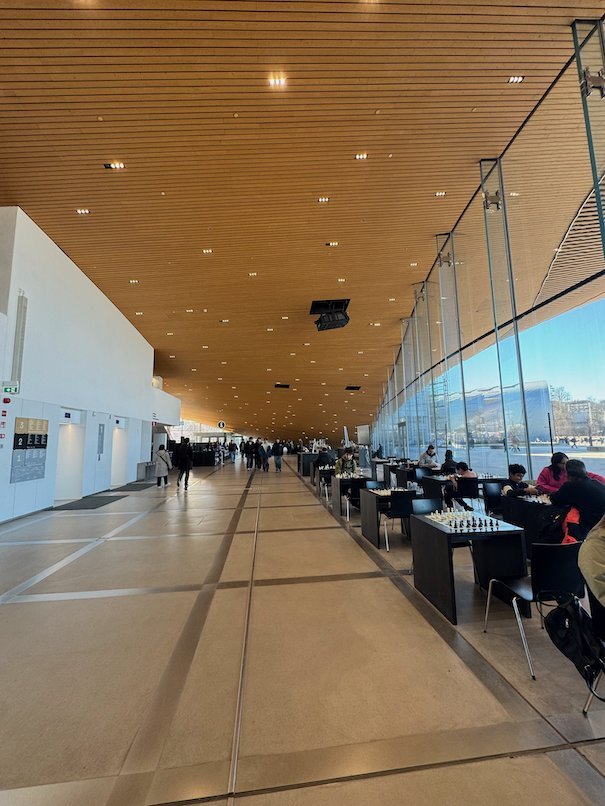 People sit at tables along a long glass wall under a wooden ceiling in Oodi library in Helsinki.