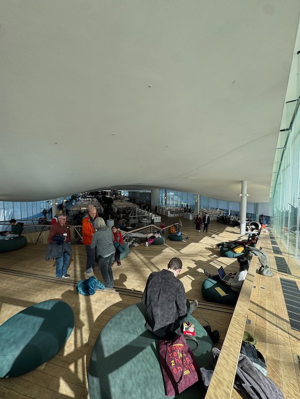 Visitors relax on seats near the large panoramic windows of the top floor of Oodi in Helsinki.