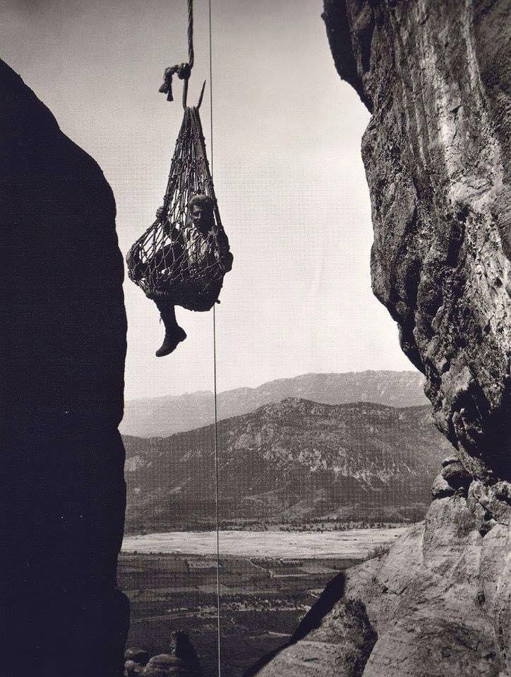 Old black and white photo of a person lifted in a rope net up the rocks of Meteora