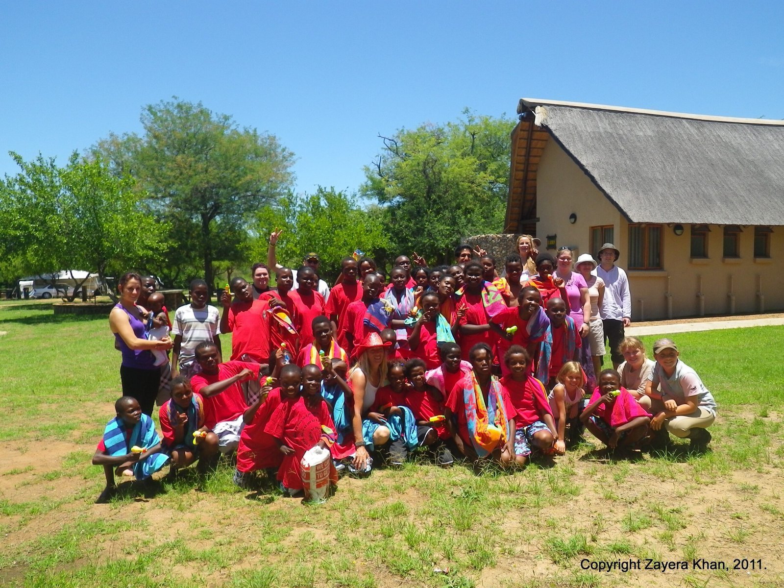 A large group of children in red shirts and visitors pose outside a school building in South Africa.