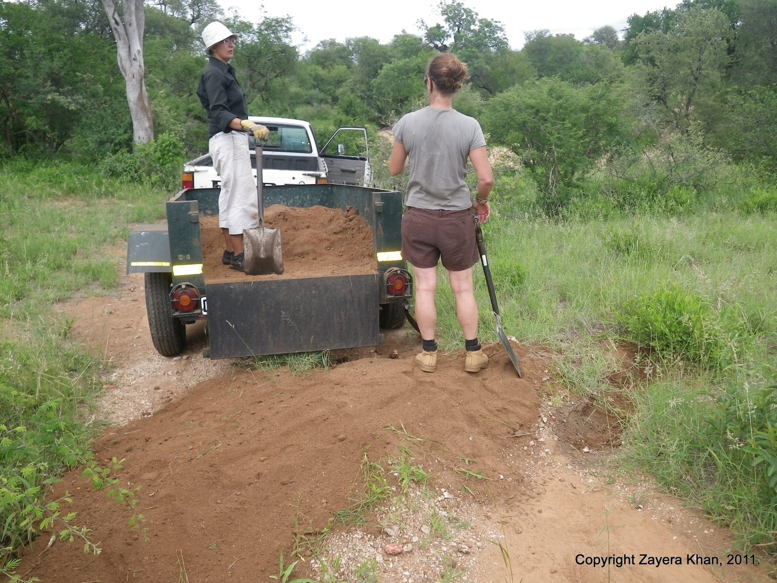 Students shovel red soil from a trailer to repair a bush road near Hoedspruit.