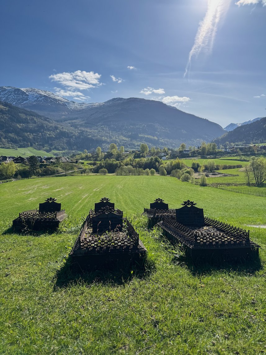 Old grave monuments in the green churchyard at Hopperstad, with mountains behind