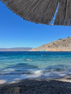 Clear turquoise water and dry hills seen from under a straw beach umbrella