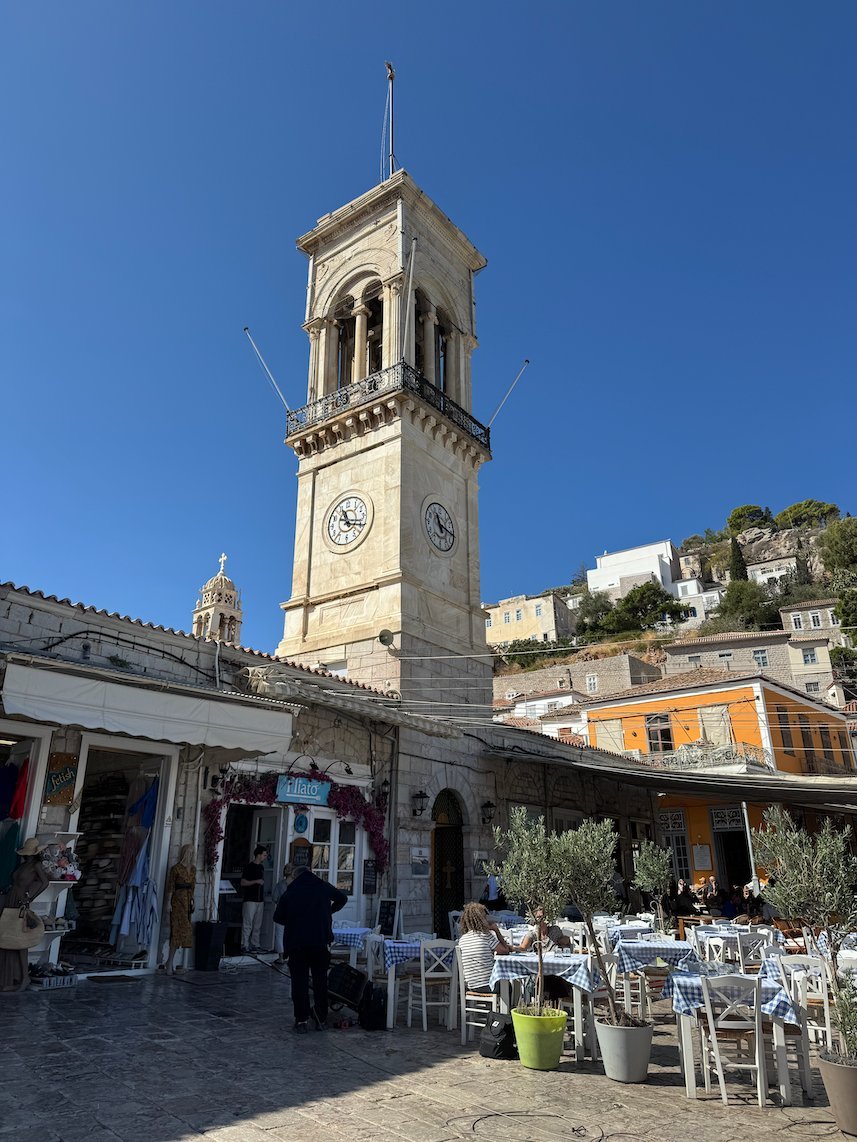 Clock tower of the cathedral above cafés at the harbor of Hydra