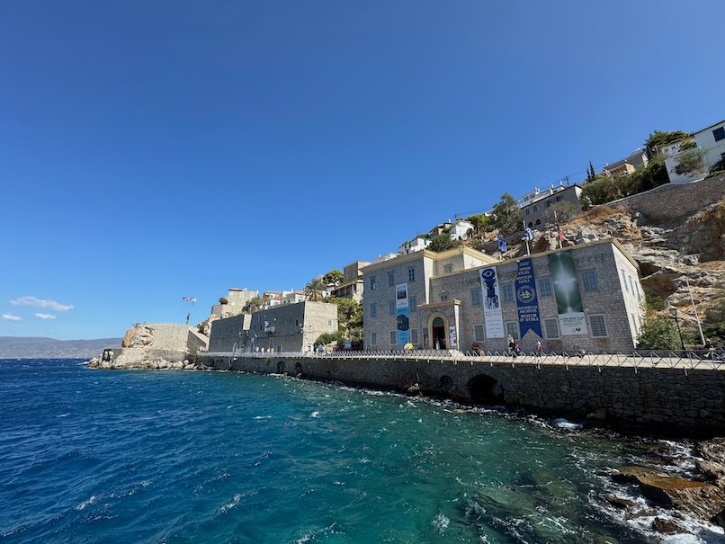 Stone buildings along the rocky coast of Hydra by clear blue water