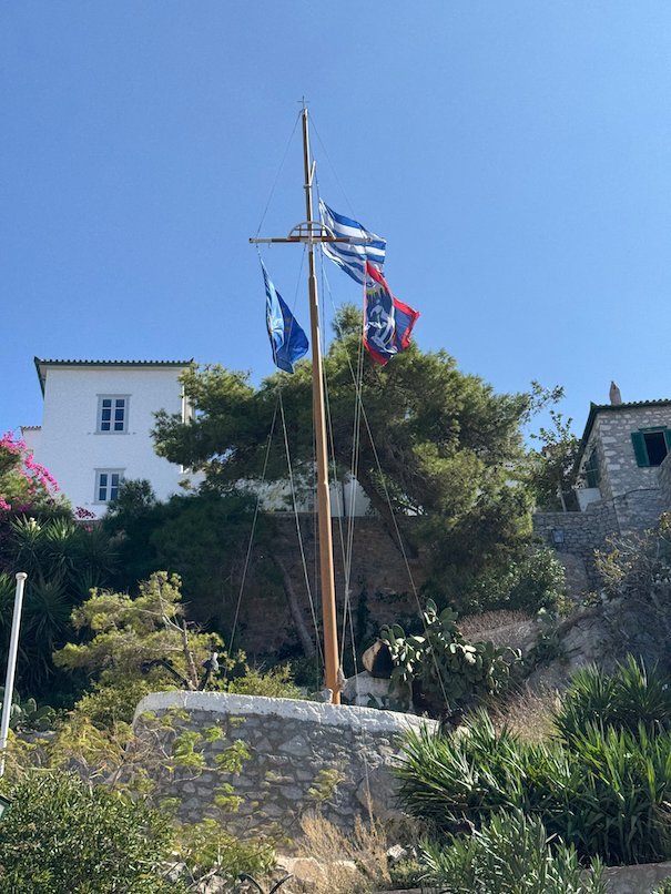 Flagpole with Greek flags among trees and old houses in Hydra