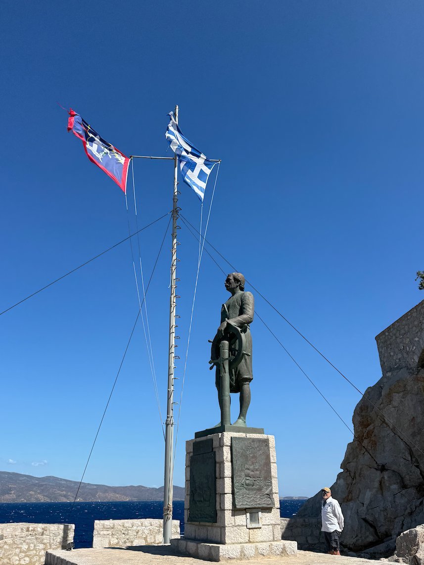 Bronze statue of Admiral Miaoulis with flags by the sea in Hydra