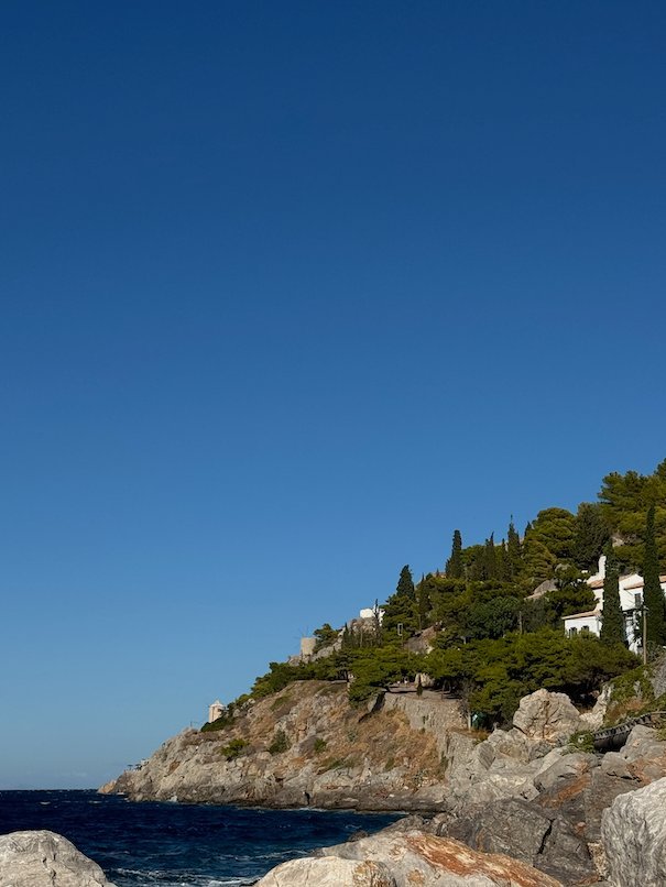 Rocky coast with pine trees and a white house above the sea in Hydra