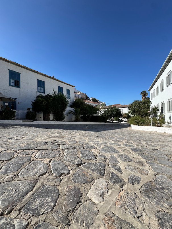 Stone paved square with white houses and green trees in Hydra
