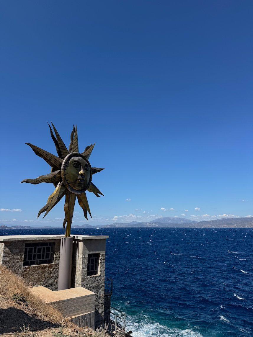 Golden sun sculpture above a stone building and the deep blue sea in Hydra