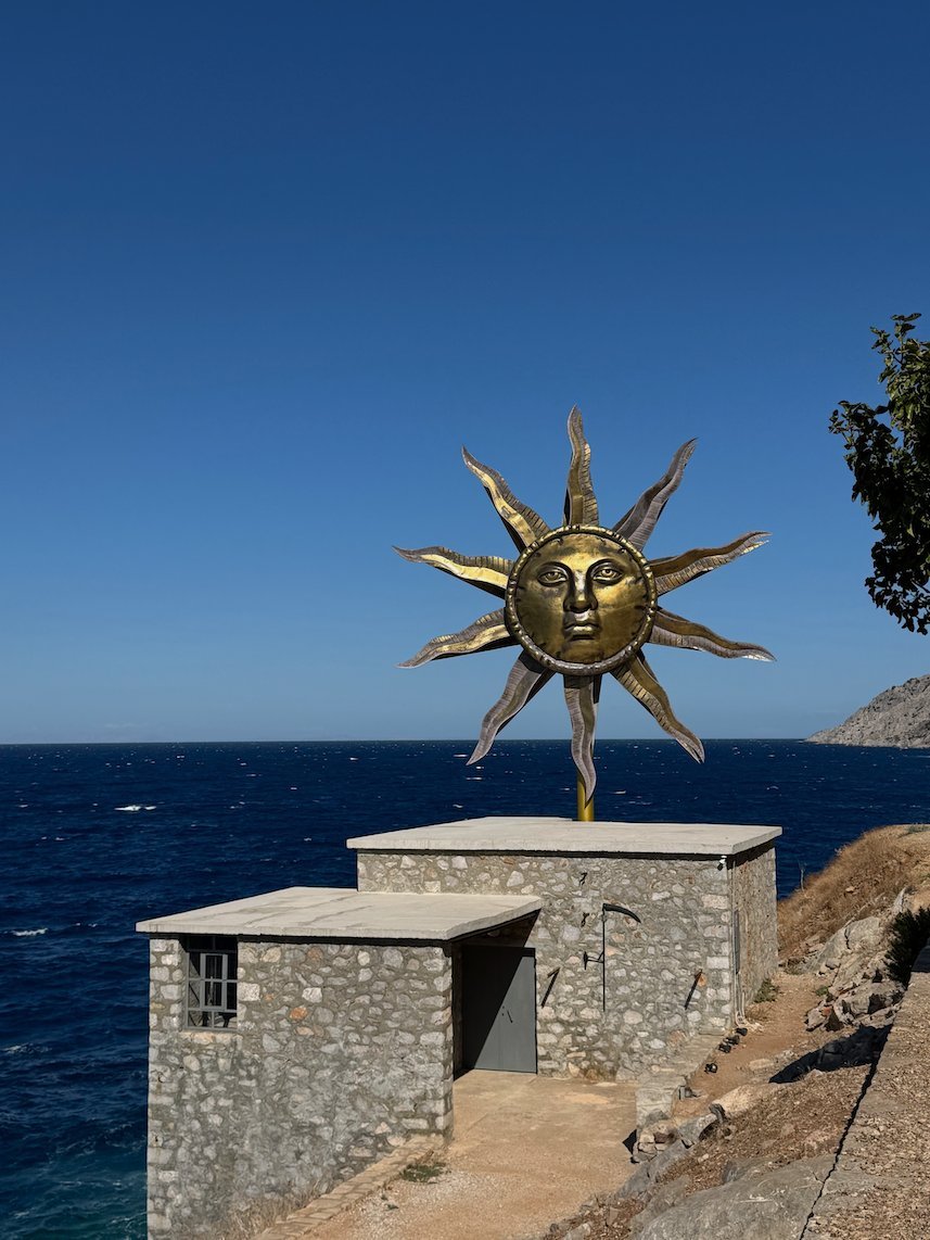 Sun sculpture on a stone house on the rocky coast of Hydra