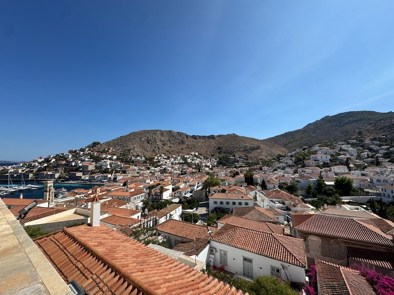 Rooftops of Hydra town and the hills behind under a blue sky