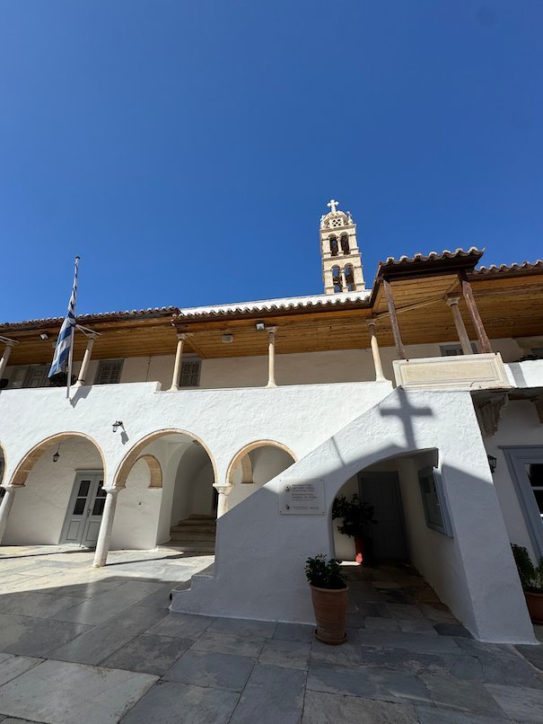 White arches, a Greek flag and a bell tower at a church in Hydra