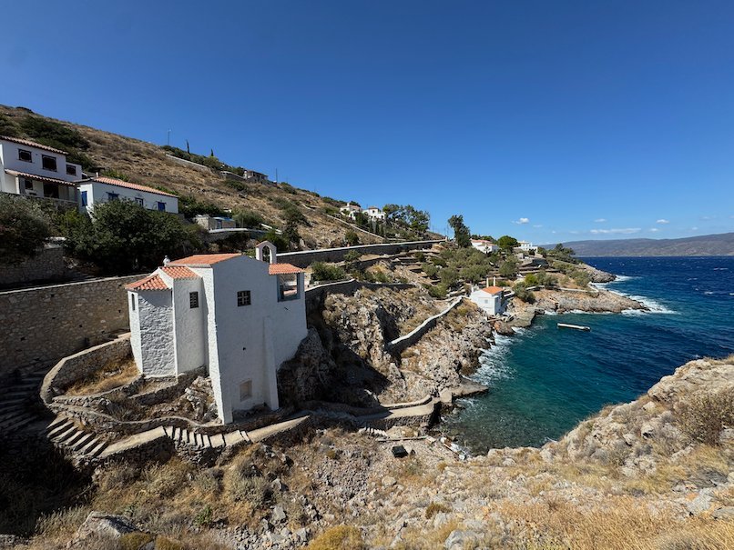 Small white building on the rocky coast with steps to the sea in Hydra