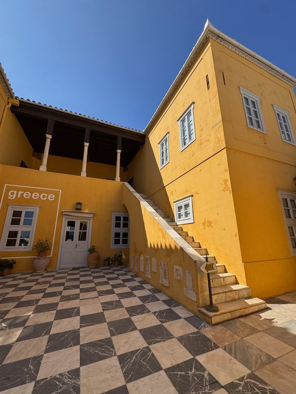 Ochre yellow mansion with a checkered courtyard and stone stairs in Hydra