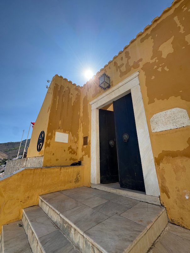 Entrance with a blue door and steps at an ochre yellow mansion in Hydra