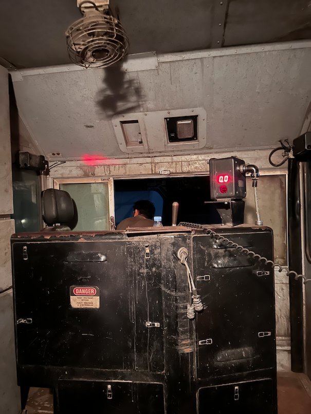 A metal box and a fan fill the inside of a locomotive cab.