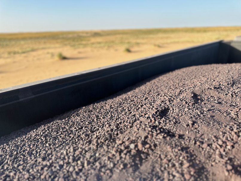 Iron ore fills a wagon as it passes green desert grass.