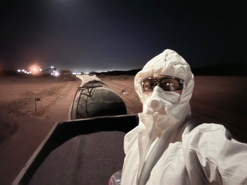 Zayera Khan in a white protective suit and mask takes a selfie at night.