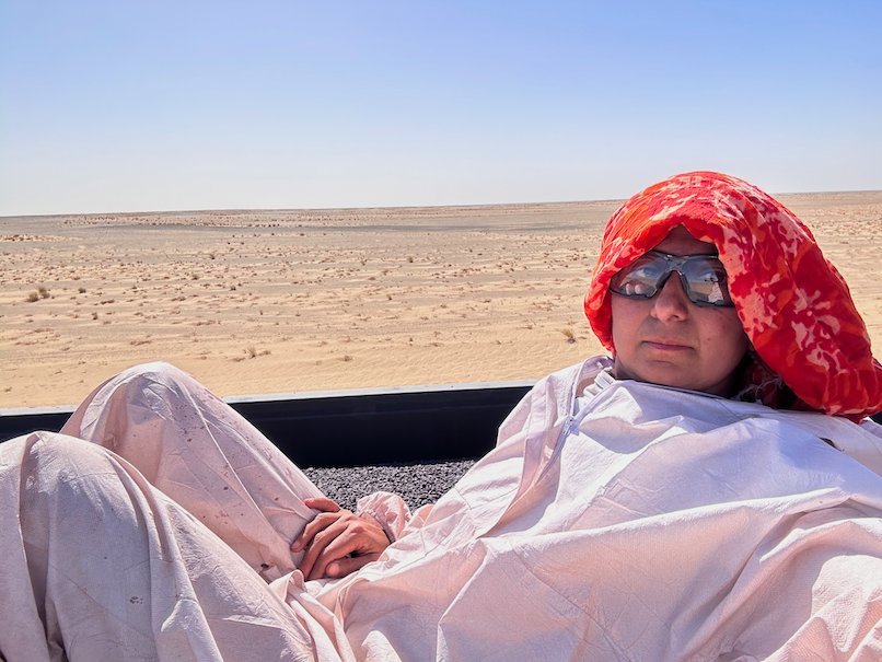 Zayera Khan in a red scarf and goggles rests on the ore wagon.