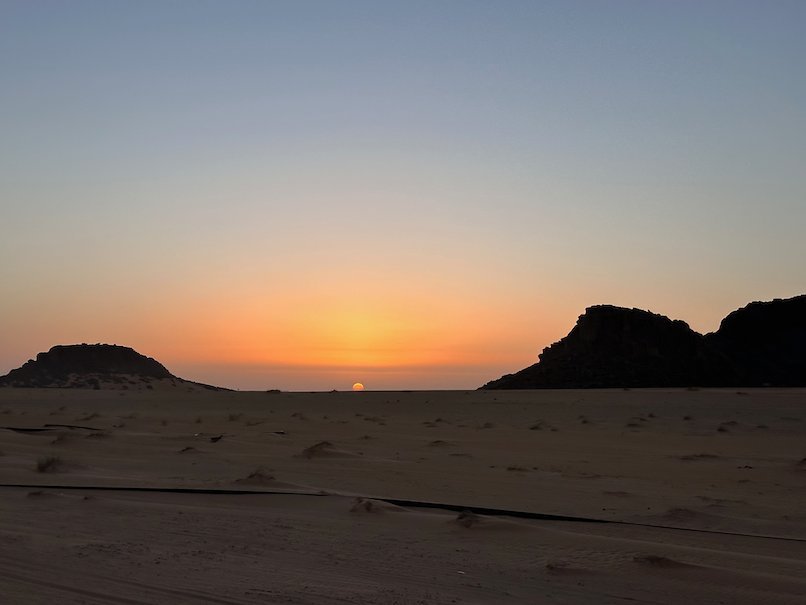 The sun rises between dark rocks over the desert.