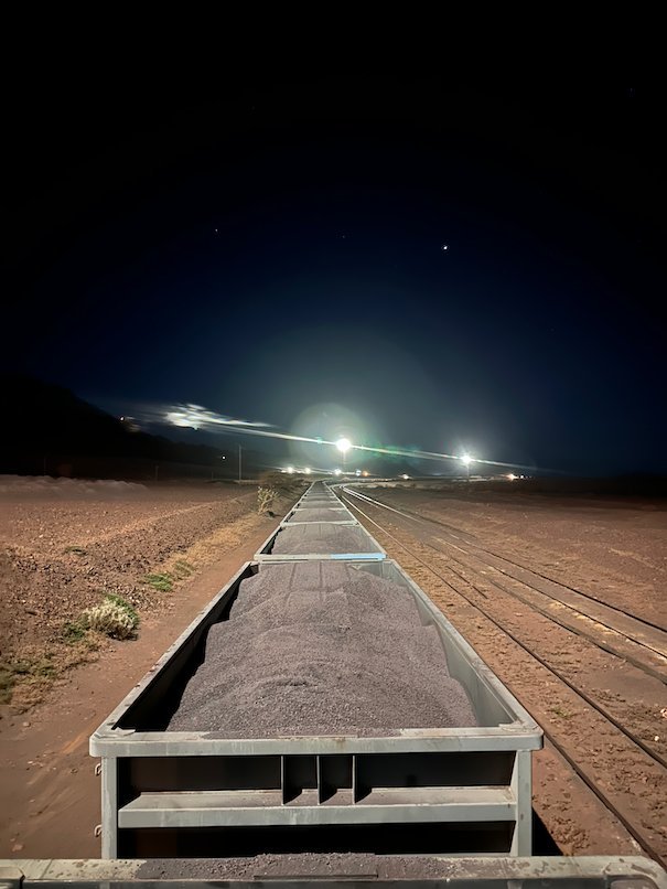 Lights shine down a long line of ore wagons at night.