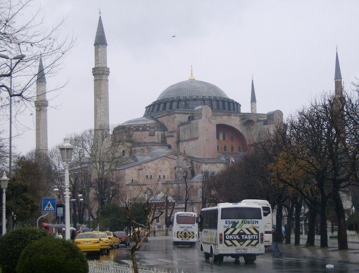 Hagia Sophia with its large dome and minarets stands beside a busy street in Istanbul.