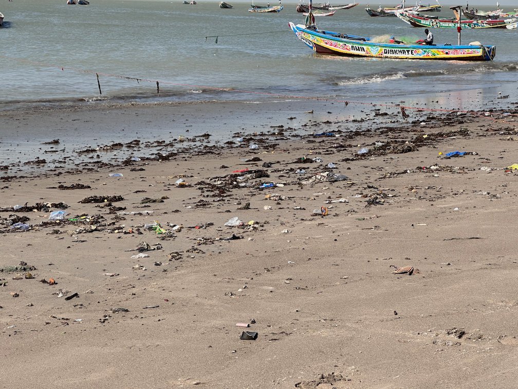 A painted pirogue lies off a beach with litter in Joal.