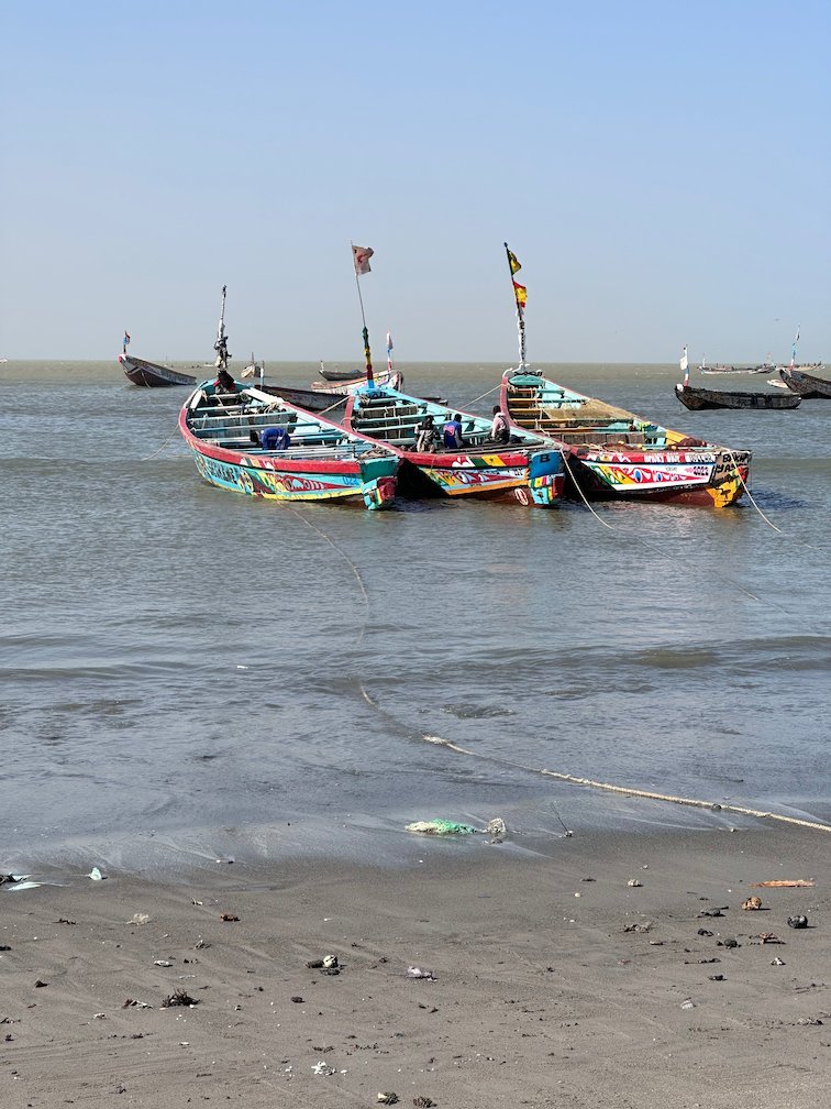 Three colorful pirogues with flags lie at the shore in Joal.
