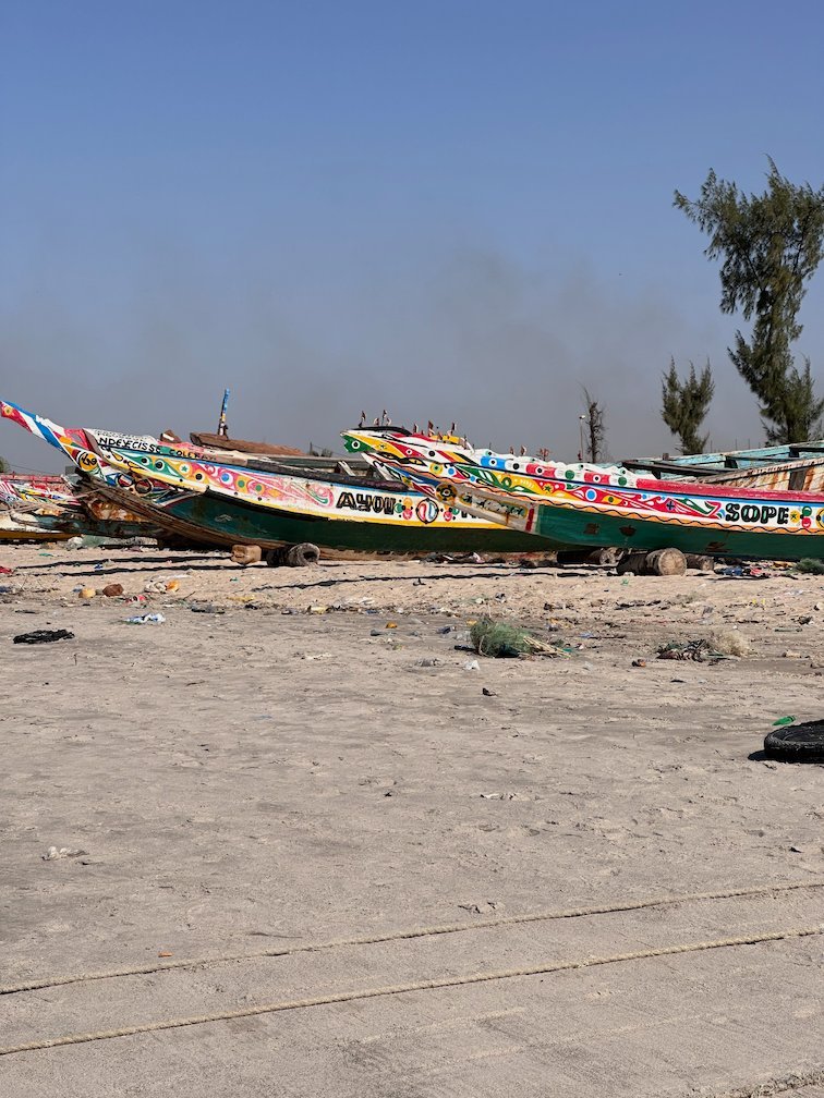 Colorful pirogues lie on the beach under smoke in Joal.