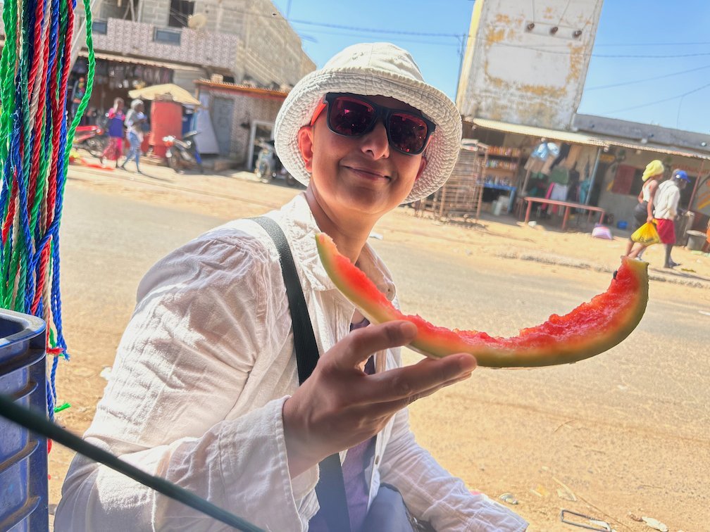 Zayera Khan holds a slice of watermelon on a street in Joal.