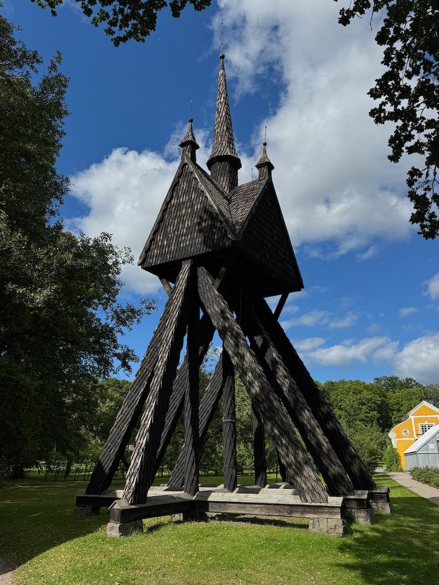Black wooden bell tower with tall spires on green grass at Julita Gård