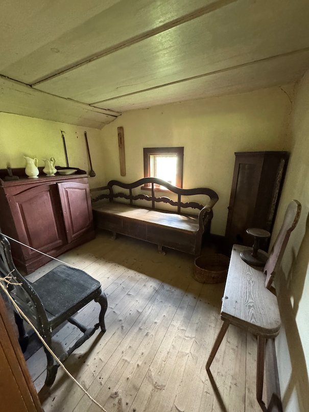Simple farmhouse room with wooden floor, a red cupboard and a wooden sofa bench
