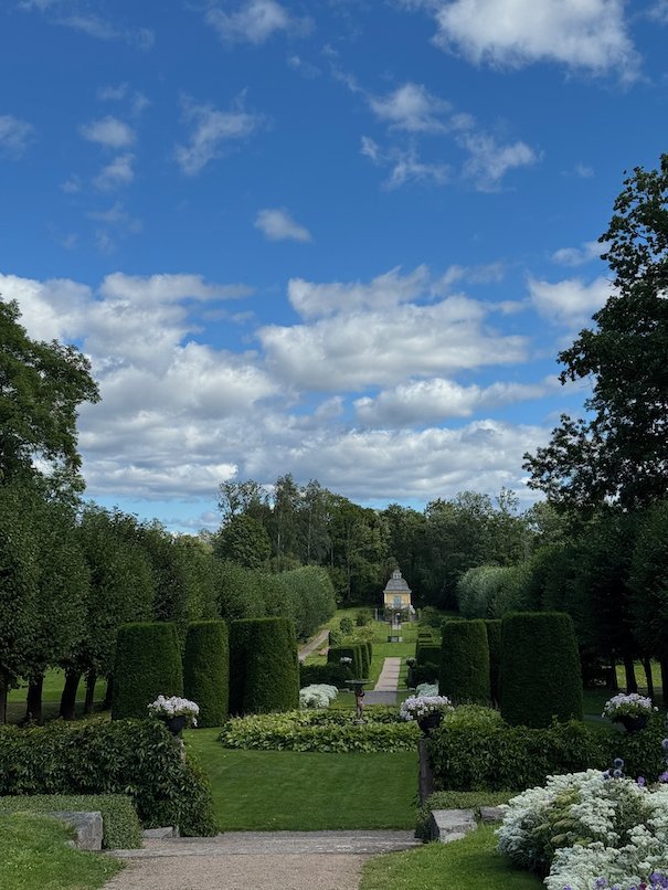 Long garden view with clipped hedges and white flowers, a small chapel at the far end