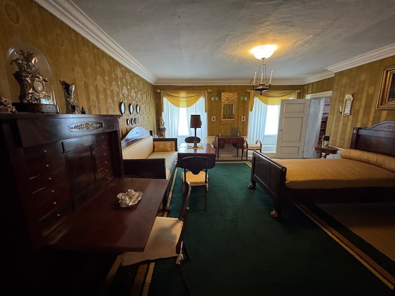 Bedroom in Julita manor with yellow walls, a green carpet, two beds and a dark wooden desk