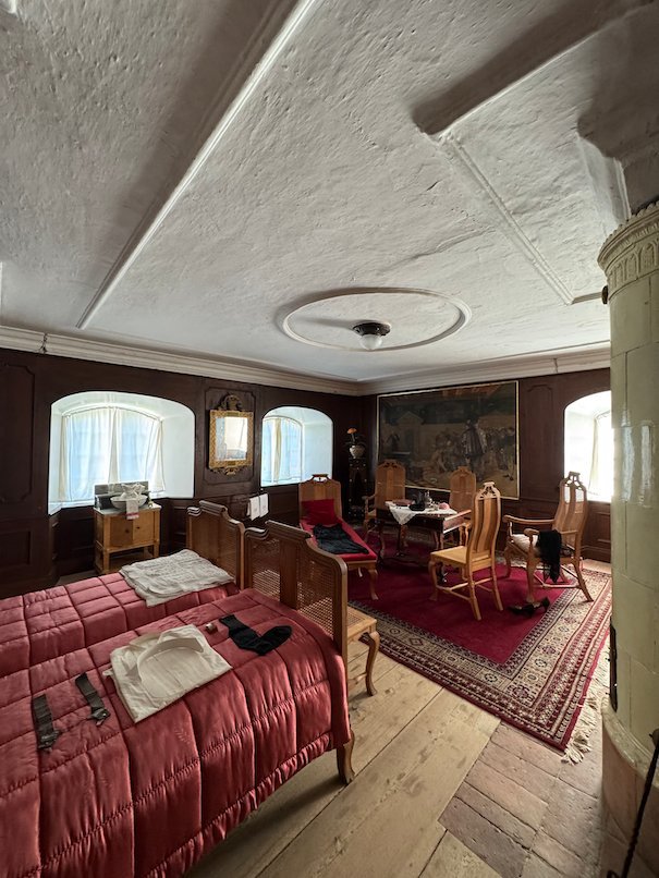 Bedroom in Julita manor with red bedspreads, a tiled stove and old furniture