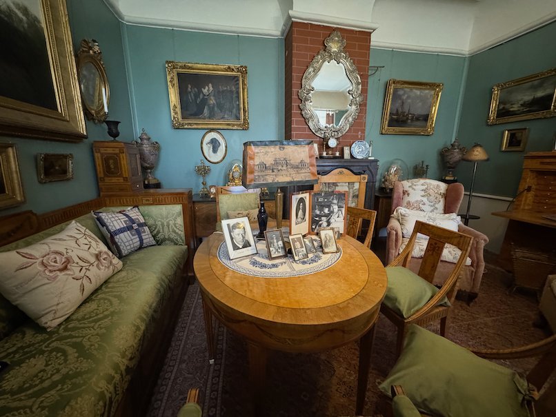 Salon with blue walls in Julita manor, with a round table, framed photos, a green sofa and a gilded mirror