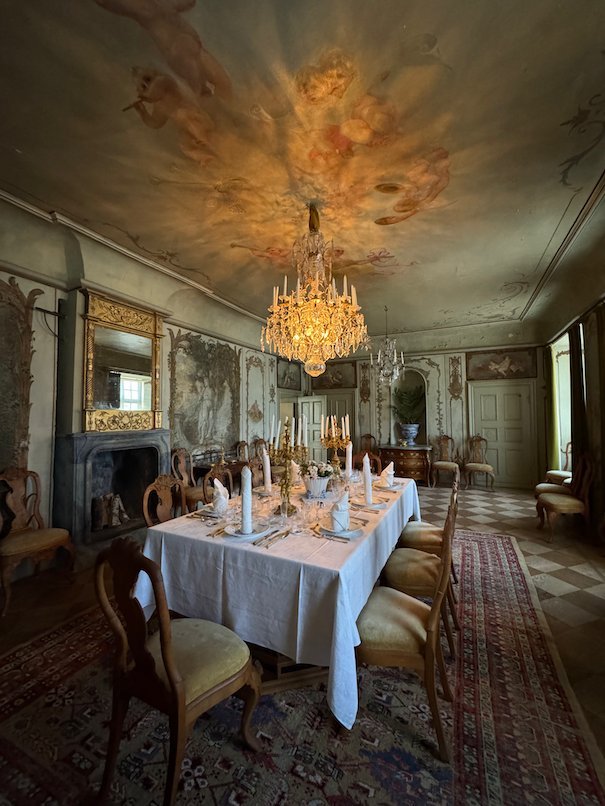 Dining room in Julita manor with a set table, crystal chandeliers and a painted ceiling
