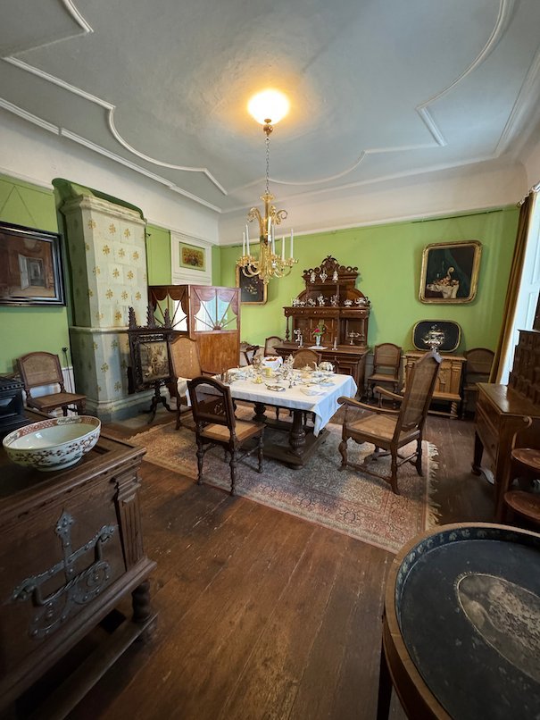 Room with green walls in Julita manor, with a tiled stove, a set table and a chandelier