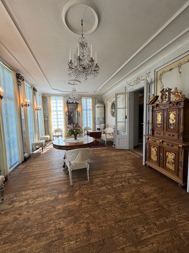 Bright hall in Julita manor with a crystal chandelier, a wooden floor and a tall carved cabinet