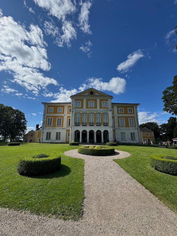 Julita Gård manor house, a yellow building with white columns, at the end of a gravel path with clipped hedges