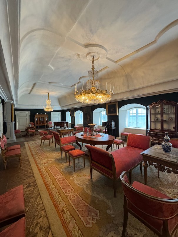 Long salon in Julita manor with red chairs, round tables and a crystal chandelier