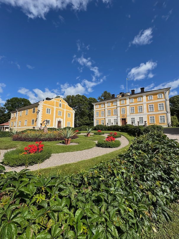 Yellow manor buildings at Julita Gård behind a formal garden with red flower beds