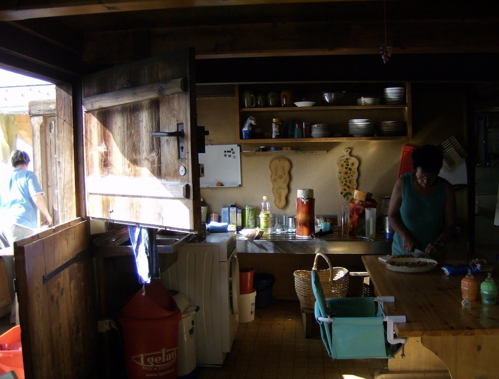 A simple kitchen with shelves and a wooden door is inside an alp farmhouse.