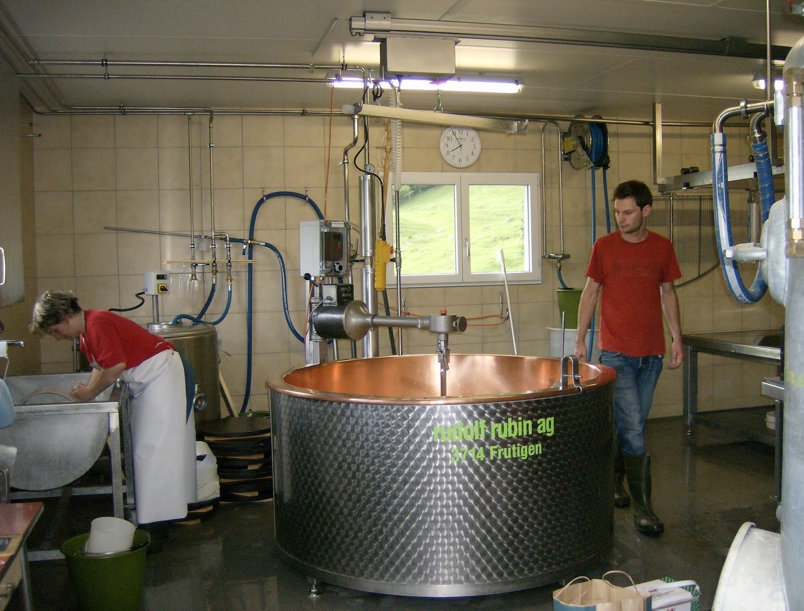 Two people work next to a large copper vat in a farm cheese dairy.