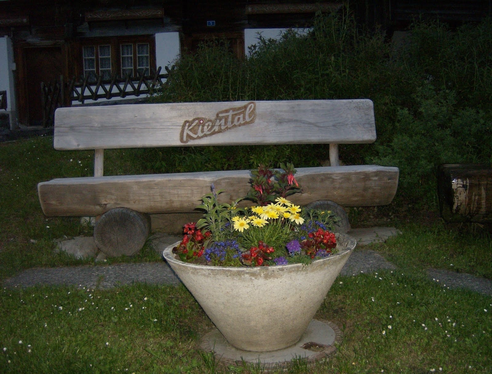 A wooden bench with the name Kiental stands behind a pot of flowers.