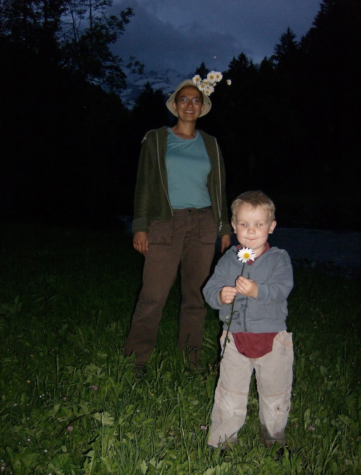 A woman and a small child stand in a meadow at dusk near Kiental.