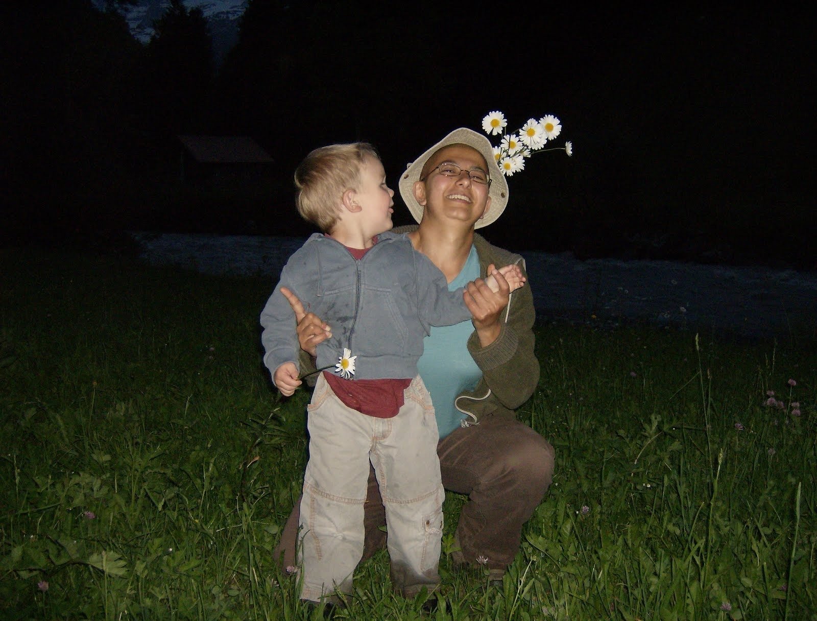A woman and a small child hold flowers in a meadow in the evening.
